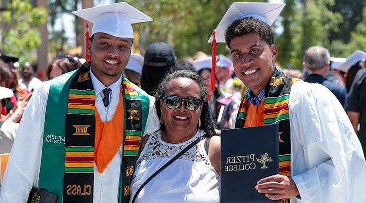 two graduates pose with a relative. One holds up their diploma.